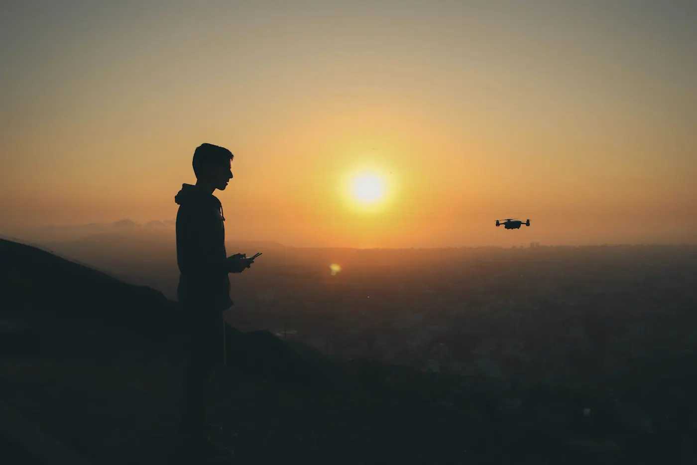 Silhouette of a drone pilot at sunset with a drone in the distance